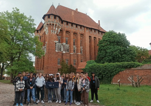 Uczniowie pozują do zdjęcia na tle zamku w Malborku.