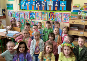 Uczniowie klasy Ia pozują do zdjęcia w wiosennych strojach, z kolorowymi pracami plastycznymi.