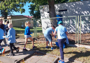 Uczniowie sprzątają teren wokół szkoły.