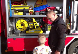 Strażak omawia dzieciom wyposażenie wozu strażackiego.